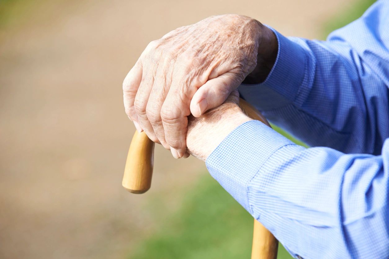 Close Up Of Senior Man's Hands Resting On Walking Stick